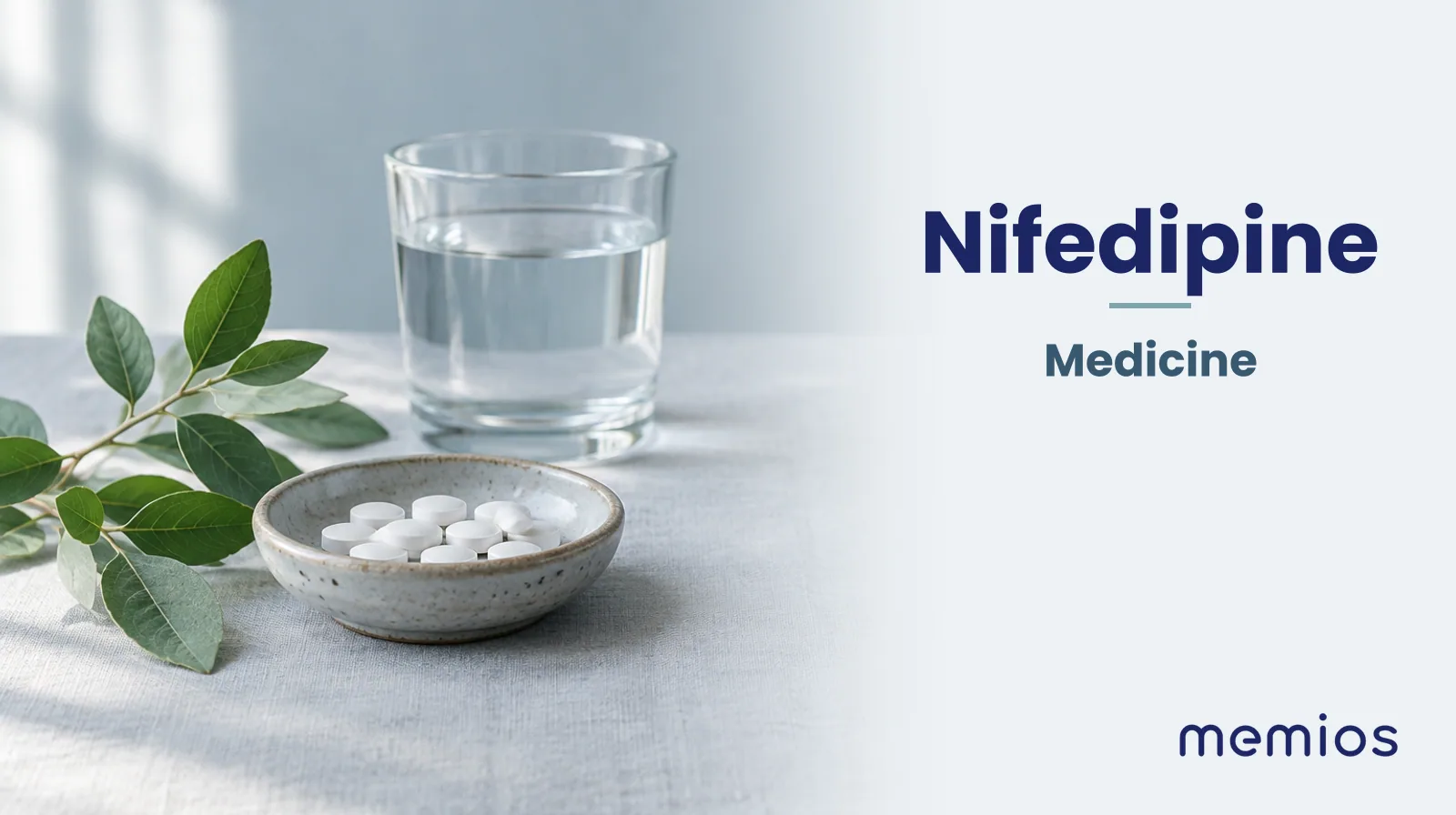 Photograph for Nifedipine: plain unmarked tablets in a dish beside a glass of water on pale linen.