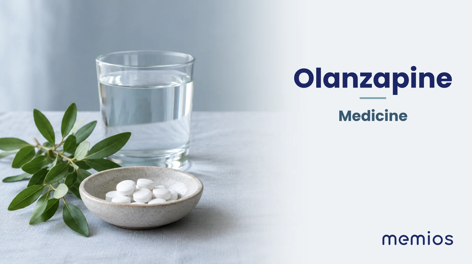 Photograph for Olanzapine: plain unmarked tablets in a dish beside a glass of water on pale linen.