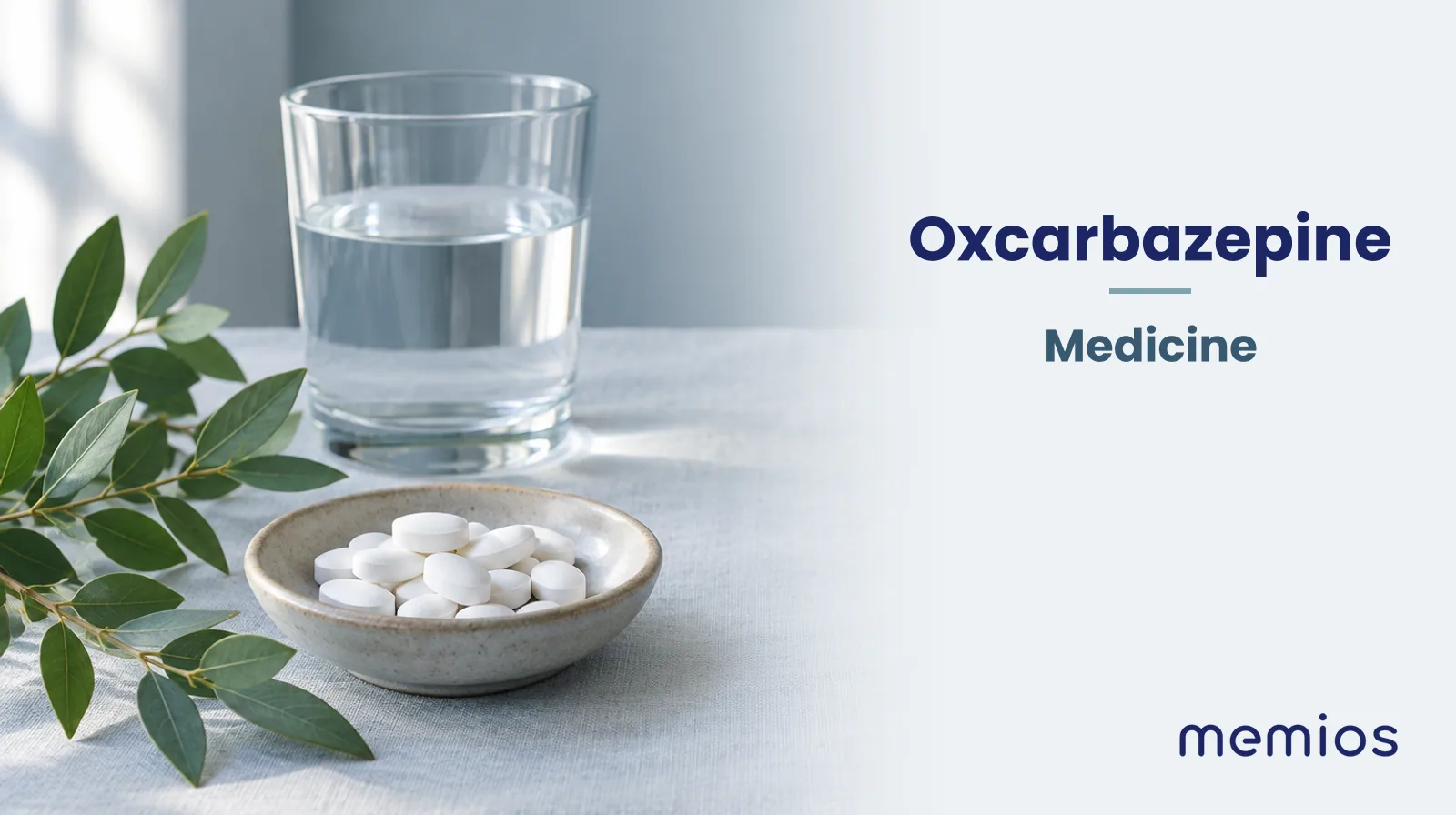 Photograph for Oxcarbazepine: plain unmarked tablets in a dish beside a glass of water on pale linen.